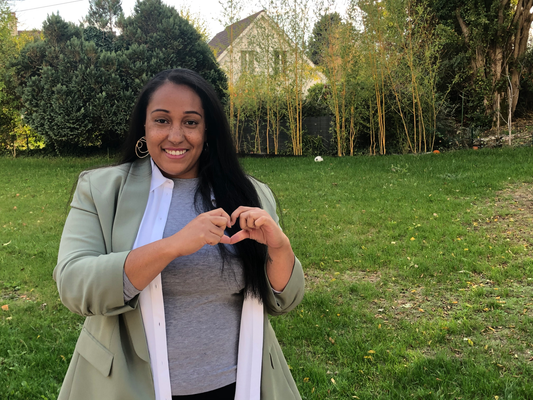 Woman in a park making a heart shape with her hands.