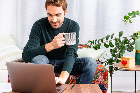 Man looking at his laptop screen while drinking from a mug.